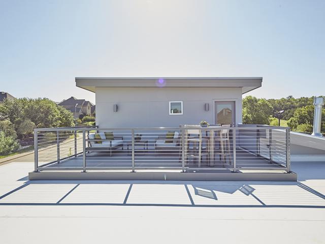 A rooftop deck perches atop the flat roof, which is covered with 60-mil fully adhered thermoplastic polyolefin (TPO) membrane roofing. Sloped roof sections are covered with an ENERGY STAR-rated Galvalume Class IV highly reflective standing seam metal roof with synthetic underlayment. The roof is designed for rainwater catchment and downspouts direct rain to a 1,500-gallon tank.