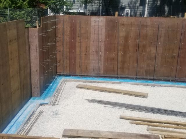 Rigid foam insulation will wrap the interior and exterior of the poured concrete walls of the home's insulated basement. The exterior surface of the walls is protected by a waterproofing coating under the rigid insulation board and a plastic dimpled drain board over the rigid foam for complete moisture and thermal protection.