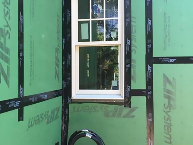 The coated wall sheathing is taped at the seams and around windows and piping to provide a continuous drainage plane under the fiber cement siding.