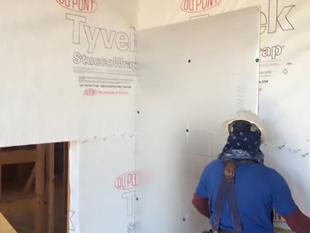 A corrugated-plastic ventilated rain screen product was installed over the house wrap to provide a ventilation gap and drainage plane behind the stucco, stone, and timber siding.