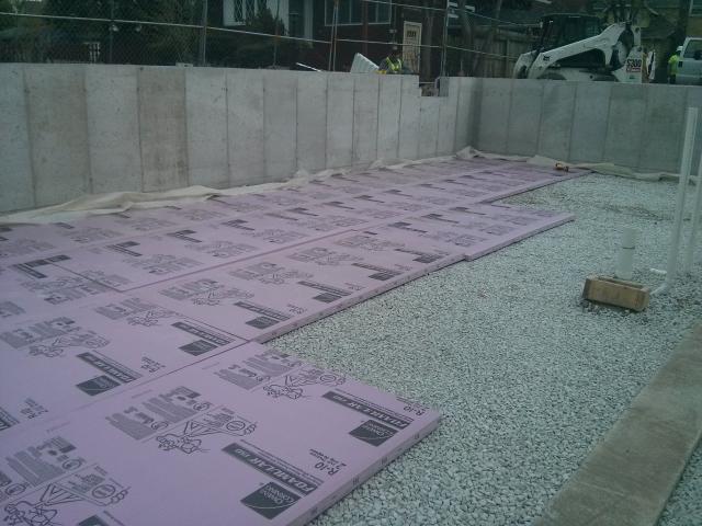 A continuous thermal blanket below the basement slab utilizes 2 inches of rigid foam insulation. This, in turn, is installed over a foundation floor water barrier system composed of a 10-mil polyethylene sheet over a gravel base; additional poly vapor barrier separates the footings from the foundation walls to keep ground moisture from migrating into walls.