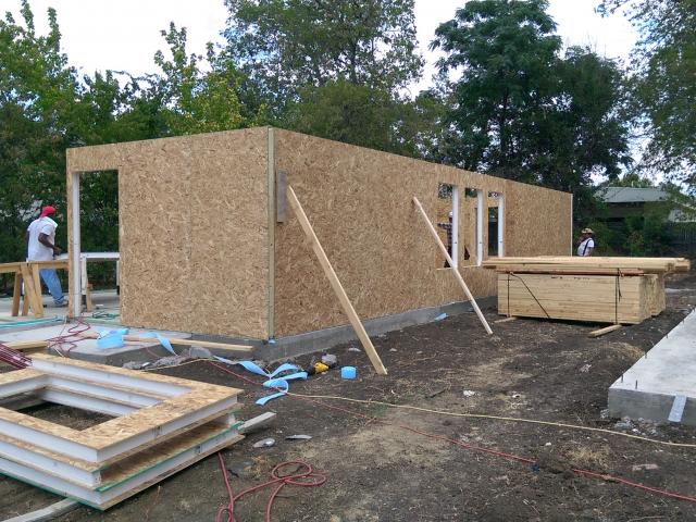 The structural insulated panel (SIP) thermal blanket uses 4.5-inch-thick wall panels (R-20) that sit on a bottom plate sealed against the post-tensioned slab foundation with a flexible foam sill gasket.