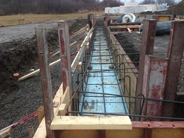 Rigid foam insulation beneath the foundation footing ties into perimeter insulation and under-slab insulation as part of a continuous thermal blanket around the building.