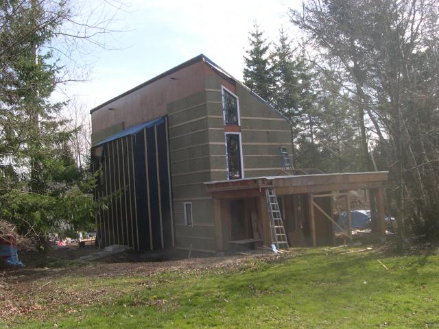 Over the 2-by-6 framing, the builder installed a continuous thermal blanket, draft protection, and water barrier consisting of plywood sheathing covered with a roller-applied elastomeric weatherproof coating, then mineral wool insulation board, then furring strips to create an air gap behind the metal and cedar siding.