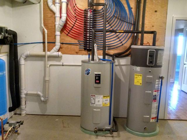 The home's ground source heat pump preheats domestic hot water for the heat pump water heater. A manifold plumbing system mounted on the wall behind the water tanks provides efficient distribution of the hot water.