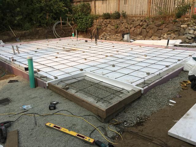 Four inches of rigid foam, a 6-mil vapor barrier, and a bed of gravel separate the ground from the slab, providing both a thermal break and a capillary break to keep the floor warm and dry.