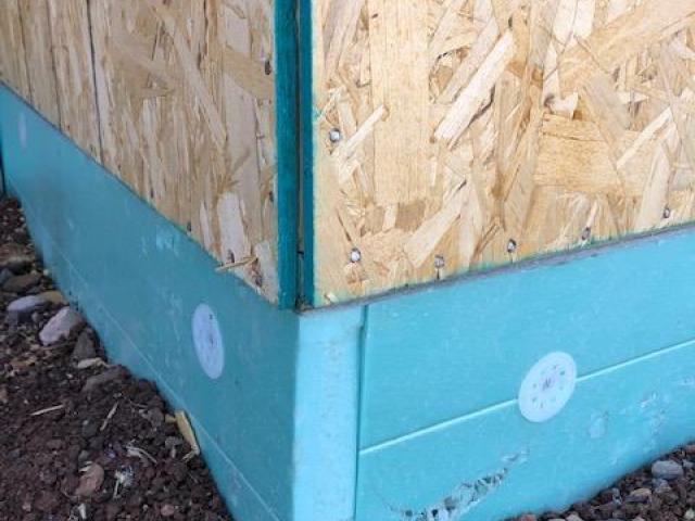 Two inches of rigid foam wraps the post-tension slab foundation in R-10 of insulation. The above-grade framed wall sill plate and sheathing overhang the slab by 2 inches, providing protection over the top edge of the foam.