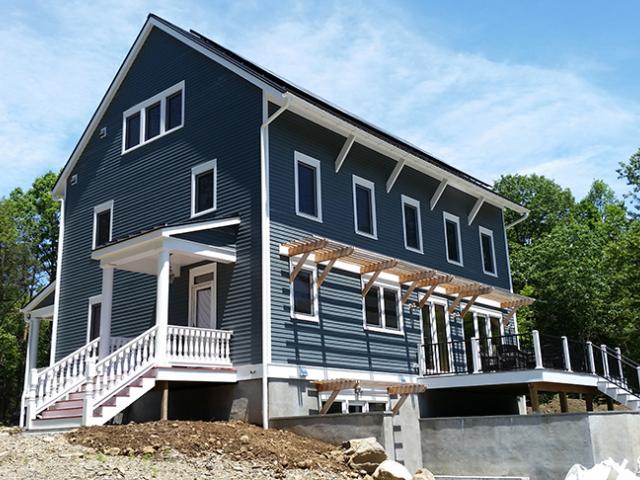 The double-stud walls are filled with 3 inches of closed-cell spray foam and dense-packed cellulose, then wrapped with a breathable vapor retarder, taped coated sheathing, a drainage mat material, and fiber cement siding to provide a durable and warm blanket of protection against the elements in this upstate New York location.