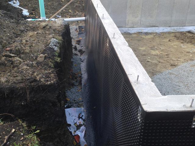 A dimpled rain mat and perforated drain pipe provide drainage around the basement foundation.