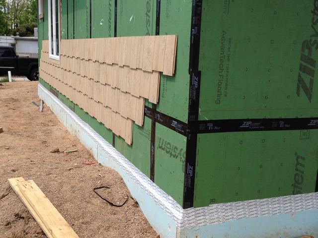 The coated OSB sheathing is taped at the seams to form a continuous air and moisture barrier behind the engineered wood siding.