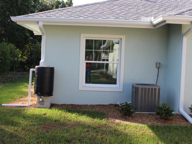 Deep overhangs, gutters, and site grading help to carry water away from the slab-on-grade foundation. A rain barrel collects some rainwater for irrigation.