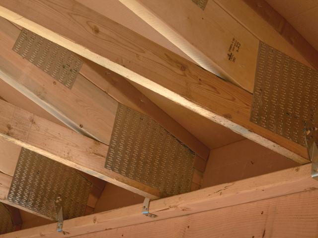 An attic comfort perimeter uses raised heel trusses that allow for a full 14 inches (R-50) of blown fiberglass at the edges of the exterior walls. Baffles keep the insulation out of the soffit vents and encourage air flow under the roof deck of the vented attic. Hurricane straps tie the roof trusses to the wall for additional wind resistance.