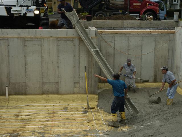 After the basement walls are set, the prepared ground is covered with 2 inches of closed-cell spray foam sprayed directly onto the 8-inch bed of trap rock. Piping for radiant floor heating is then laid down and covered with the concrete slab floor.